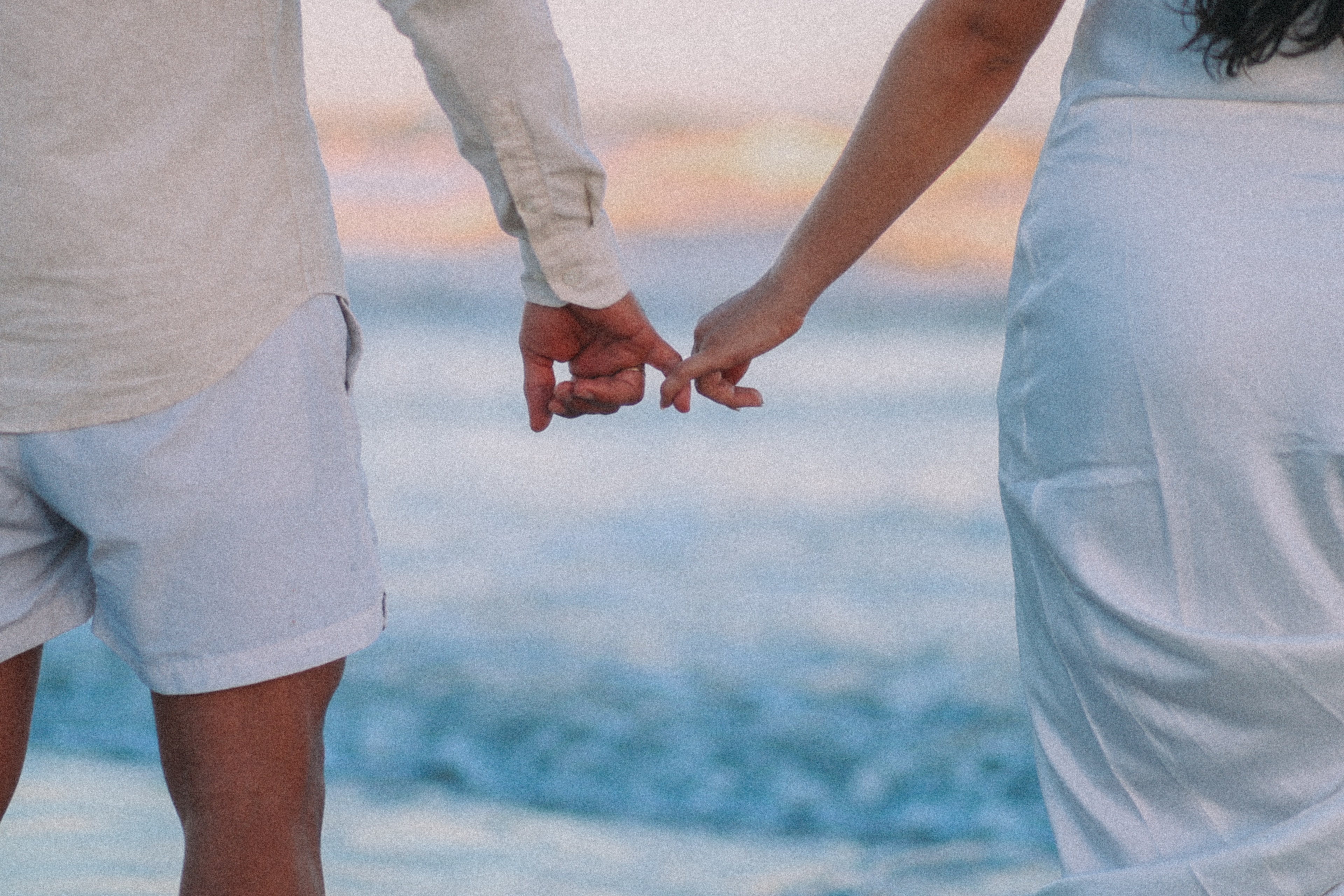 Mãos do casal entrelaçadas na praia